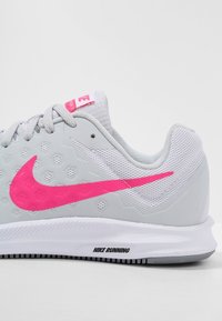 Scarpa da corsa grigia con dettagli rosa, tomaia in mesh testurizzato, suola in gomma e grande logo Nike swoosh. Presenta un sistema di chiusura con lacci e branding.