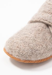 Szary-brązowy filcowy kapcie z teksturowaną powierzchnią, gumową podeszwą i designem z krzyżowym paskiem. Miękki, przytulny materiał do użytku wewnętrznego.