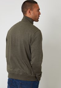 Sudadera de color verde oliva, de manga larga, con cuello alto, puños y dobladillo acanalados; tejido suave con un diseño minimalista, vista desde la parte de atrás.
