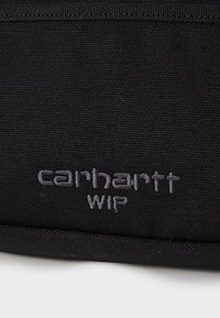 Borsa nera in tessuto con logo ricamato "carhartt WIP" in grigio. Il materiale è testurizzato e resistente, con un design semplice e rettangolare.