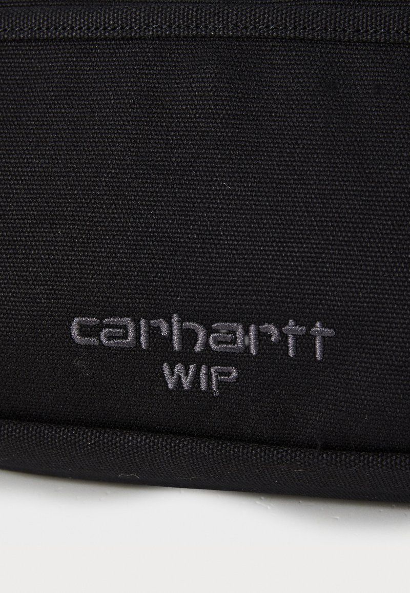 Bolsa de tela negra con un logo de "carhartt WIP" bordado en gris. El material es texturizado y duradero, con un diseño simple y rectangular.