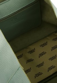Interieur van een groene leren handtas met een ritsvak en een gladde, beige voering met herhalende "Venezia" branding.