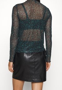 Transparent långärmad topp med en teal- och brun leopardmönster, kombinerad med en kort svart läderkjol som tillför en mjuk textur.