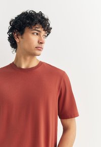 Rozsdabarna, rövid ujjú póló puha anyagból, kerek nyakkivágással és letisztult, sima textúrájú minimalista dizájnnal.