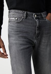 Grå denimjeans med klassisk passform. Har sølvfarge detaljer, glidelås foran, fem lommer og en subtil falmet tekstur på stoffet.