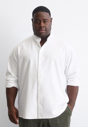 White long-sleeve shirt with a stand collar and rolled-up sleeves. Smooth fabric with button closures and a relaxed fit.