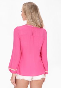 Blusa rosa a maniche lunghe in tessuto testurizzato, con chiusura a bottoni sul retro e rifiniture a contrasto sulle maniche.