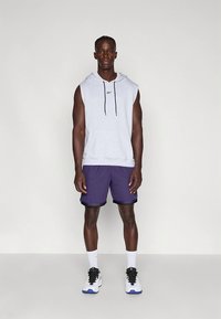 Szara bezrękawnikowa bluza z kapturem z czarnymi sznurkami, w zestawieniu z fioletowymi siateczkowymi szortami. Białe skarpetki i czarne buty z niebieskimi akcentami dopełniają stylizację.