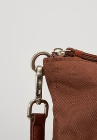 Gros plan d'un coin de sac en tissu marron avec un clip de fermoir argenté fixant une sangle en cuir à un anneau en métal.