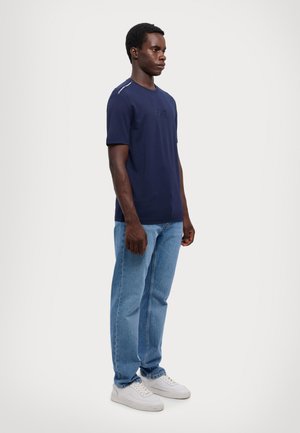 Camiseta de algodón azul marino de mangas cortas con un logotipo sutil. Combinada con jeans de mezclilla azul claro y zapatillas blancas.