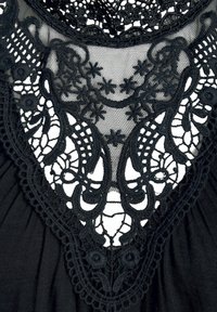 Schwarzer Spitzenstoff mit kunstvollen floralen und geometrischen Mustern, mit gewelltem Rand und geschichteter Textur, präsentiert auf einem glatten Hintergrund.