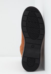 Bruine suède laars met een gestructureerde zwarte rubberen zool, met een licht gebogen vorm en zichtbare stiksels langs de zijkant.