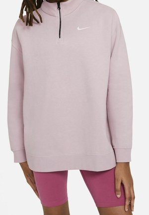 Personne portant un sweat Nike rose clair à demi-fermeture éclair et un short de cyclisme rose foncé, visible des épaules jusqu’au milieu des cuisses.