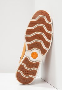 Semelle de chaussure beige et blanche avec motif d'adhérence texturé, logo circulaire orange et étiquette "SensorFlex" sur une surface lisse.