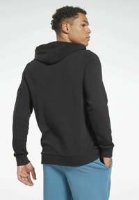 Sudadera negra con bolsillo canguro, puños y dobladillo acanalados. Tejido suave, estilo de sobrecamisa, con capucha ajustable y corte relajado.