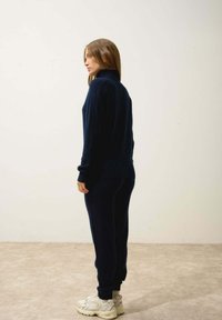 Granatowy dres z dzianiny z wysokim kołnierzem i ściągaczami, w połączeniu z jasnymi trampkami. Gładka tekstura i dopasowany krój.