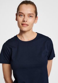 Marinblå t-shirt i bomull med rund hals, korta ärmar och en figurnära silhuett. Slät textur, minimalistisk design utan mönster.