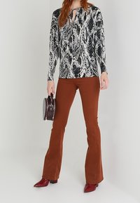 Czarny i biały top w wężowy wzór z długim rękawem i dekoltem w kształcie łezki, w połączeniu z brązowymi spodniami dzwonami i czerwonymi butami na szpilkach. Dołączona mała torebka.