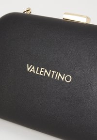 Svart läderclutch med en slät yta, försedd med en guldfärgad VALENTINO-logotyp och en metallisk låsdetalj. Kompakt rektangulär form.