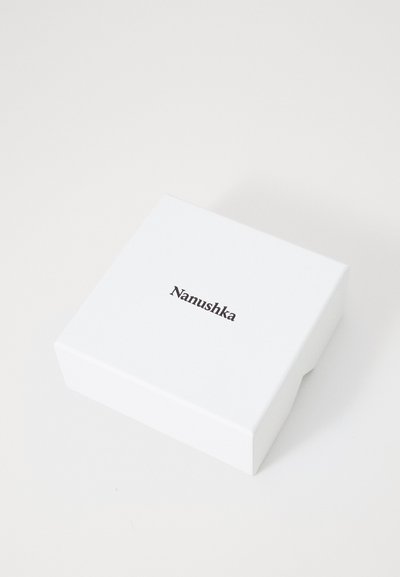 Valge ristkülikukujuline kast sileda pinnaga. Sõna "Nanushka" on peal trükitud minimalistlikus mustas fondis.