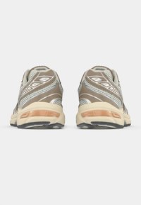 Zapatillas de correr en beige y gris con parte superior de malla, diseño curvado, suelas acolchadas y detalles reflectantes en los laterales y la parte trasera.