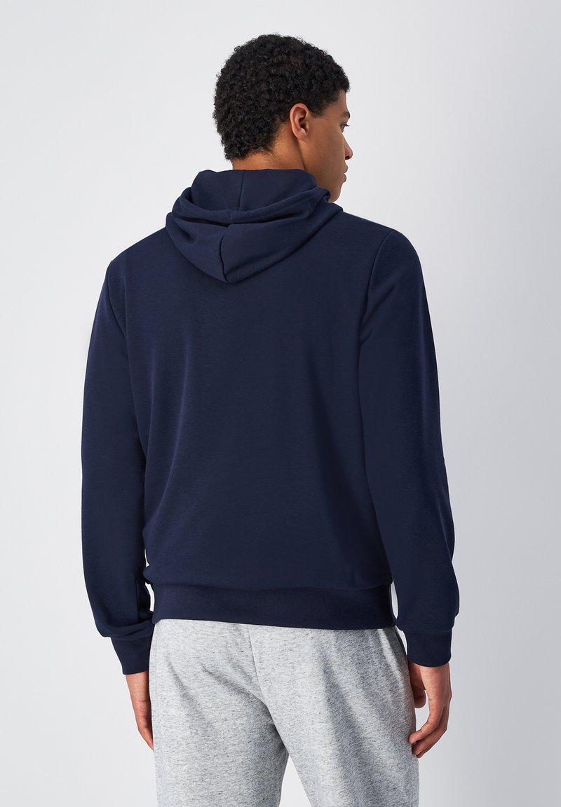 Felpa blu navy con tasca a marsupio, cappuccio con cordino e polsini a costina, abbinata a pantaloni grigi. Tessuto morbido, design casual.