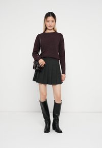 Suéter de malha em borgonha, saia mini plissada preta e botas pretas até ao joelho. Pequena bolsa preta com detalhe de fivela.
