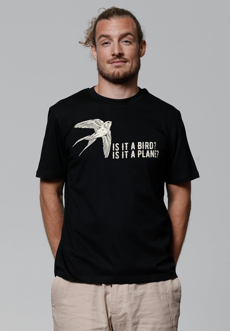 Zwarte katoenen t-shirt met een grafiek van een vliegende vogel en de tekst "Is het een vogel? Is het een vliegtuig?" in lichtgekleurde letters. Eenvoudig ontwerp.