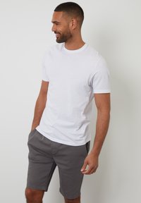 T-shirt en coton blanc avec un col rond, associé à un short gris. Le short est fabriqué dans un tissu léger et comporte des poches latérales.