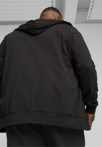 Sort pullover hoodie med hætte, der har en afslappet pasform, glat tekstur og en lige kant. Set fra ryggen har den lange ærmer.