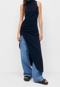 Vestido sin mangas de color marino con detalles fruncidos en los laterales, combinado con jeans de pierna ancha de color azul claro y sandalias de plataforma negras. Texturas suaves en toda la prenda.