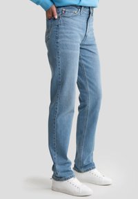 Jeans de denim de color azul claro con corte recto, que cuentan con un diseño clásico de cinco bolsillos y un ligero desgastado. Combinados con zapatillas blancas.
