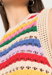 Primo piano di un top all'uncinetto multicolore con strisce orizzontali di crema, rosso, lilla, blu, verde, rosa e giallo sulla parte superiore del petto e sul collo di una persona.
