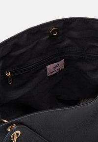 Borsa a tracolla nera in ecopelle con una texture liscia, dotata di una chiusura a scatto in metallo dorato e una tasca interna con zip etichettata "ANNA FIELD."