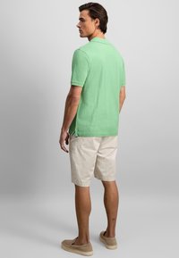 Chemise polo vert clair à manches courtes et fentes sur les côtés, associée à un short beige. Le tissu semble doux et décontracté.