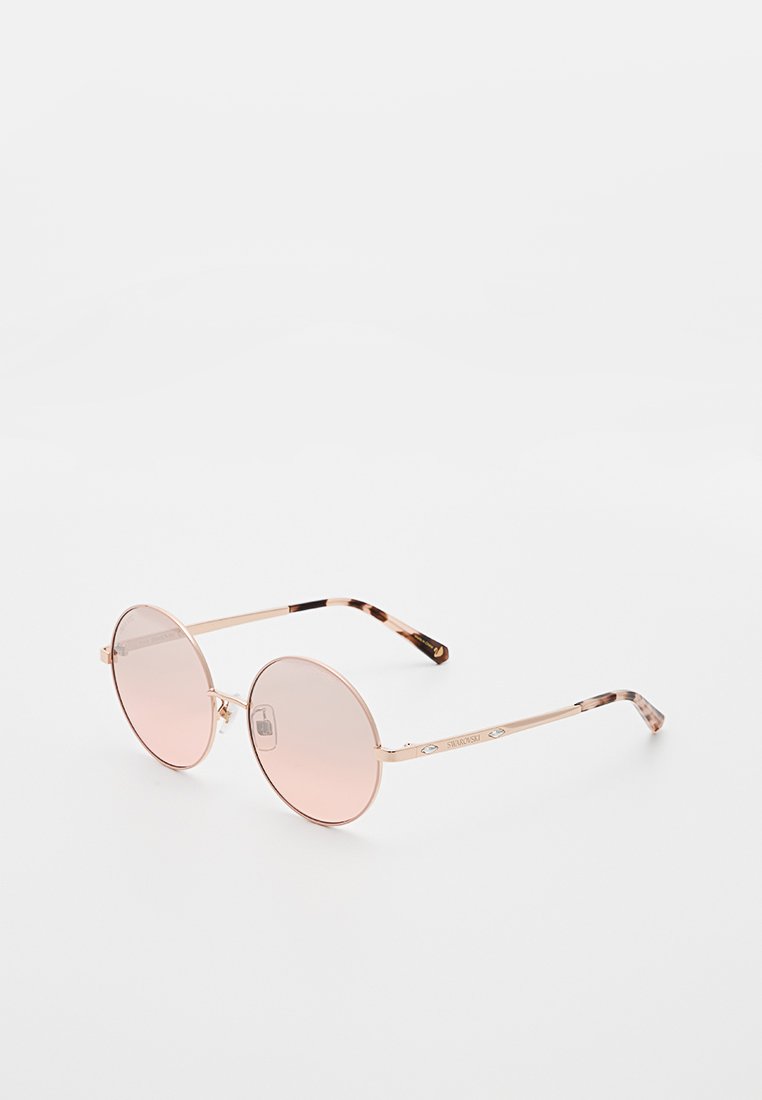Lunettes de soleil rondes avec des verres rose clair et une monture en métal doré rose. Accentuation avec un motif écaille sur les branches.