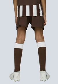 Brunt fotbollskit med randig tröja, matchande shorts, vita strumpkantar och vita fotbollsskor med Puma-logga. Slätt, atletiskt material.