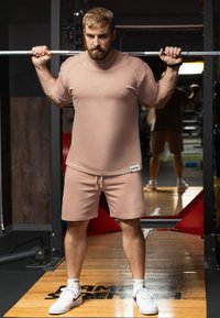 Tenue de sport rose pâle comprenant un t-shirt ajusté à manches courtes et un short assorti. Le tissu semble doux ; le t-shirt comporte un logo discret et le short est doté d'un cordon de serrage.