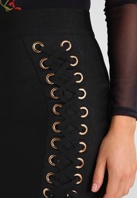 Falda negra de cintura alta, con un diseño de cordones y ojales dorados en el costado. Confeccionada en un material ajustado y texturizado.
