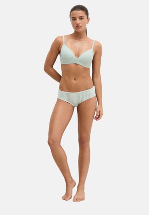 Woman standing with one hand behind back, wearing light mint green striped bra and matching high-waisted briefs against a plain background.