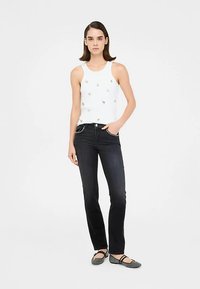 Camiseta blanca sin mangas con adornos coloridos, combinada con jeans vaqueros oscuros y zapatos planos grises. Diseño plano, corte ajustado y textura suave.