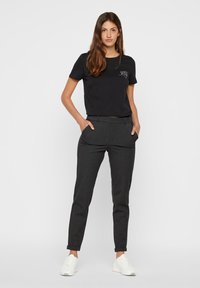 T-shirt nero a maniche corte con una piccola grafica, abbinato a pantaloni grigi a sigaretta con tasche laterali e orli risvoltati. Sneakers bianche.