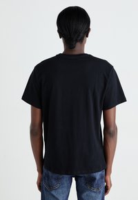 Sort bomulds T-shirt med korte ærmer og rund hals, der har et ensfarvet design med en lige kant, vist fra ryggen.