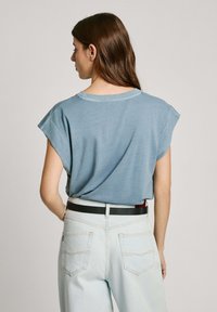 Šviesiai mėlynas trumpomis rankovėmis marškinėliai su laisvu kirpimu ir apvalia iškirpte, derinami su aukštu liemeniu šviesiais džinsais ir juodu diržu.