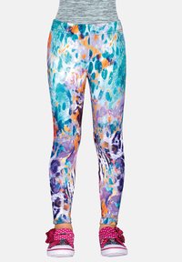 Jaskrawe, wielokolorowe legginsy z abstrakcyjnym wzorem noszone z różowymi butami w kropki, ozdobionymi kokardkami i błyszczącymi akcentami.