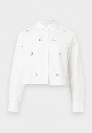 Chemise blanche à manches longues cropped avec col, boutonnée à l'avant, ornée de petites fleurs dorées éparpillées sur le devant et les manches.