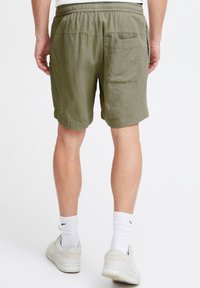 Pantaloni scurți kaki confecționați din material texturat, cu talie elastică, având un buzunar în spate și tiv răsucit. Purtate cu șosete albe și pantofi.