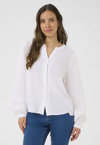Camicia bianca a maniche lunghe con apertura frontale a bottoni, dettagli in pizzo delicato lungo la patta e le maniche, realizzata in tessuto leggero.