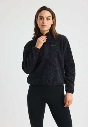 Zwarte fleece pullover met luipaardprint, hoge kraag, halve rits aan de voorkant en logodetail. Draag het over zwarte leggings met een gladde textuur.