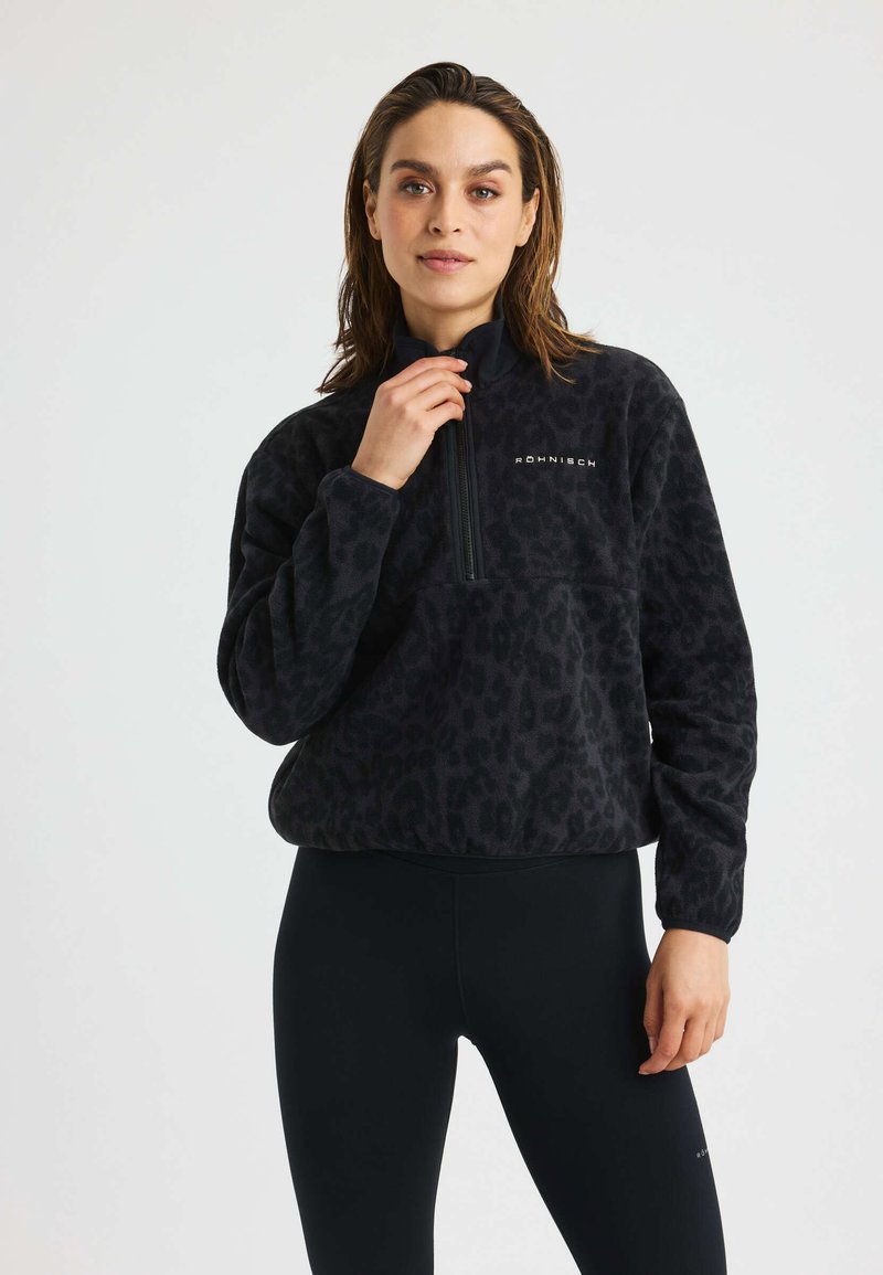 Pullover in pile nero con stampa leopardata, colletto alto, zip frontale a metà e dettagli con logo. Indossato sopra leggings neri, texture liscia.